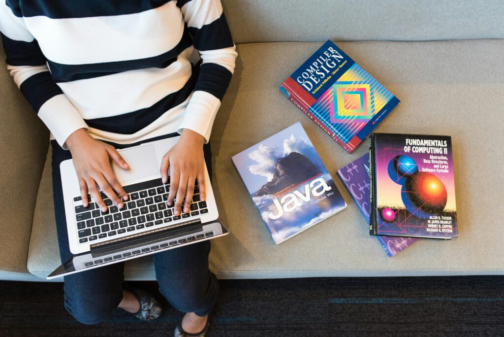 Best Tech Skills to Learn in Nigeria This Year and Why Woman using laptop on sofa, surrounded by programming books, learning coding.