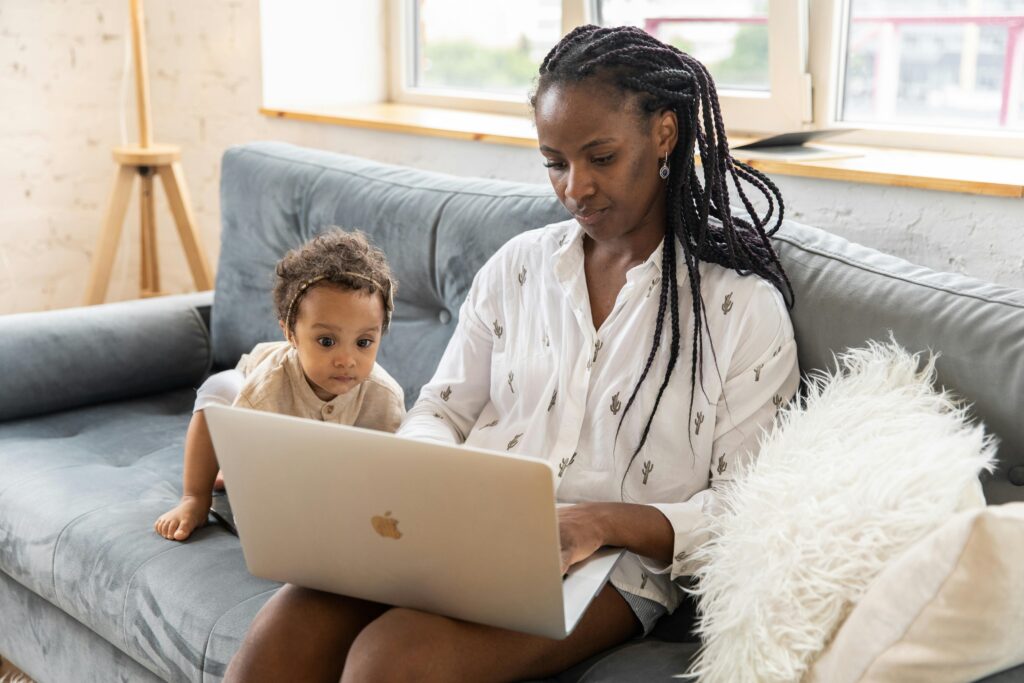 Mother and baby sitting on the sofa using a laptop together indoors, showcasing modern family life.
