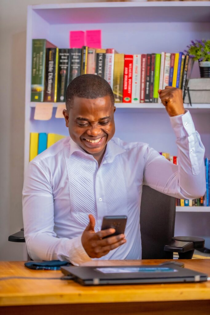 African man celebrating success on mobile phone in a vibrant home office.